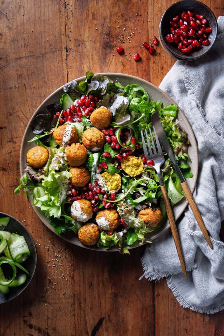 Falafel Salat mit Granatapfelkernen, Gurke und Tahini-Dressing – Food-Fotografie von knusprigen Kichererbsenbällchen auf frischem Blattsalat in rustikalem Setting