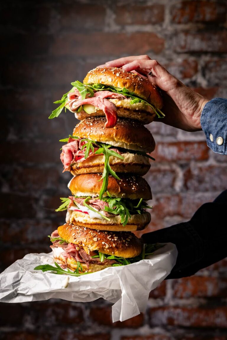 Gourmet Roastbeef Sandwich mit Rucola und Sesam-Bun – Food-Fotografie eines gestapelten Deli-Burgers im rustikalen Ambiente mit Brick-Wall Hintergrund