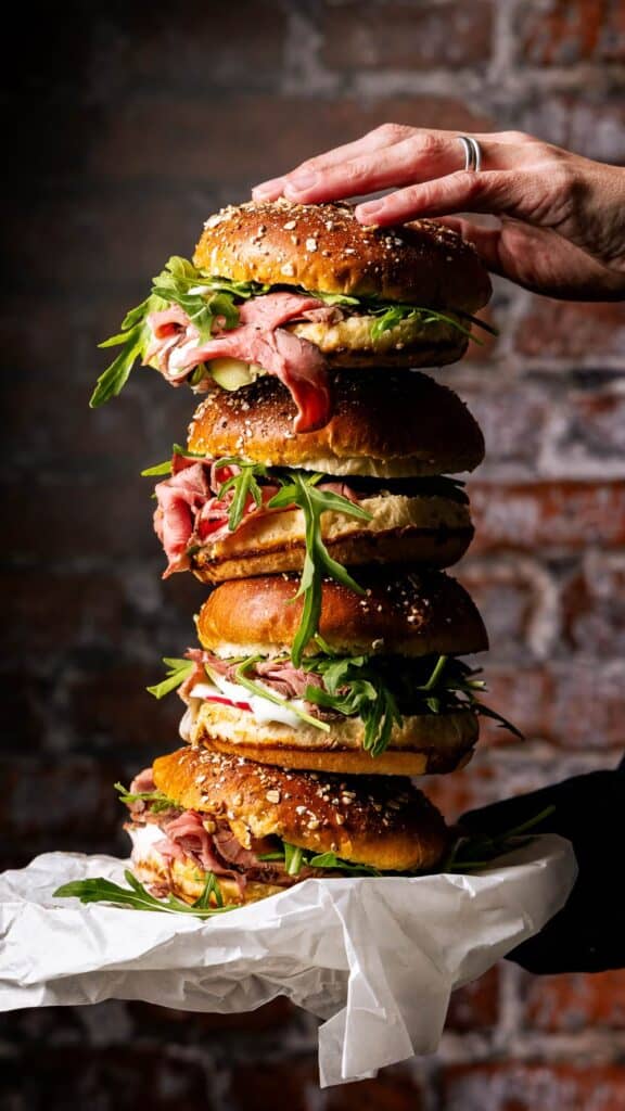 Gourmet Roastbeef Sandwich mit Rucola und Sesam-Bun – Food-Fotografie eines gestapelten Deli-Burgers im rustikalen Ambiente mit Brick-Wall Hintergrund