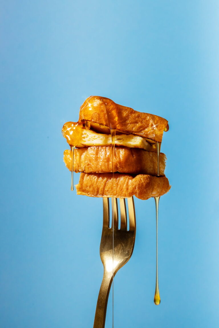 Commercial Food Photography eines French Toast Sandwiches mit geschmolzener Butter und fließendem Honig auf einer Gabel vor blauem Hintergrund – moderne, luxuriöse Food Brand Bildsprache